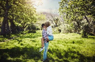 Couple, park and kiss in nature with love, hug and commitment together outdoor. Girlfriend, boyfriend and people with care, romance and anniversary or engagement date outside relaxing and bonding