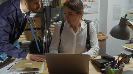 A man and woman in an indoor detective office environment, analyzing evidence on a laptop