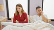 © Krakenimages.com - A woman and man sit apart in bed, portraying tension in a modern bedroom, hinting at relationship issues.
