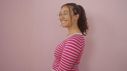 Poster - A cheerful young hispanic woman in a striped shirt posing with glasses against an isolated pink wall.