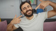 © Krakenimages.com - Smiling bearded man pointing at himself in a cozy living room setting, embodying positivity and confidence.