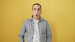 © Krakenimages.com - Surprised young hispanic man in a gray shirt against a vibrant yellow background, exuding expressive charm.