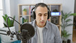© Krakenimages.com - Hispanic man speaking into microphone in a radio studio with headphones and on-air sign.