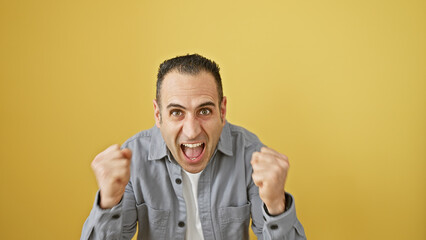 Wall Mural - Excited man cheering in triumph, with a bright yellow background, portraying emotions of success and joy.