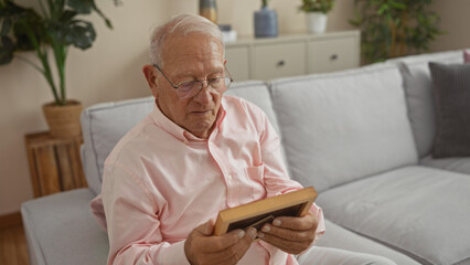 Middle-aged caucasian man holding a picture frame while sitting on a couch in a well-decorated living room at home.