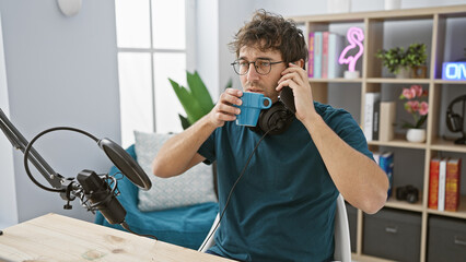 Hispanic man drinking coffee while talking on phone in a modern radio studio setting