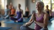 © Athena - A serene older woman practices yoga in a group class, demonstrating mindfulness and tranquility in a bright studio setting.