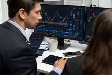 Two business traders discussing on dynamic stock market in currency rate investment trading on two pc screens with compare real time graph on risk or profit point of data at modern office. Postulate.