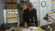 © Krakenimages.com - A focused woman detective examines documents in a cluttered police station office, hinting at a complex investigation.
