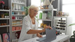 © Krakenimages.com - Woman smiling while working with laptop in home decor store, surrounded by various colorful decorations and plants