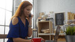 © Krakenimages.com - Young woman with red hair on phone looking at laptop in an indoor bakery setting