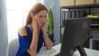 © Krakenimages.com - Young woman sitting in an office focusing on her computer screen and looking stressed during work
