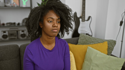 Indoor portrait of a thoughtful african american woman sitting in a modern living room at home.