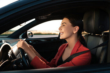 Canvas Print - Smiling young woman with seatbelt driving car, view from outside