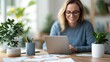 © Pinklife - A joyful woman in glasses works from home on her laptop, surrounded by plants and stationary, conveying feelings of comfort, productivity, and a home-like work environment.