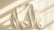 © R&R Studio - White knitted sweater laid flat on a beige surface, with long sleeves and a V neck, with light and shadow.