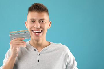 Wall Mural - Happy young man with teeth color samples on light blue background, space for text. Dental veneers