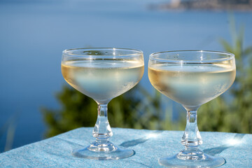 Wall Mural - Cold sparkling wine, cava or champagne in two coupe glasses on table with blue sea water view