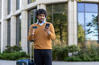 © Liubomir - Confident man outside modern building using smartphone and holding credit card. Concept of online shopping, travel, and technology. Carrying suitcase, blending business urban environment.