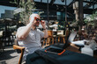 © qunica.com - Businessman at an outdoor cafe working on a laptop, adjusting his sunglasses, participating in a business meeting, and enjoying the sunny day.