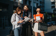 © qunica.com - Three businesswomen discussing documents and charts outdoors. Collaborative work atmosphere during the golden hour in an urban setting.