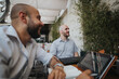 © qunica.com - Young business entrepreneurs strategizing and collaborating on a project at an outdoor cafe, focusing on teamwork for improvement and growth.