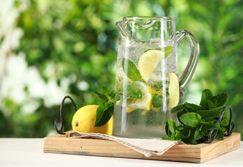 Wall Mural - Refreshing lemonade with mint in jug and citrus fruit on light table against blurred green background, closeup