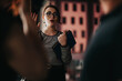 © qunica.com - A young professional woman engaging in a dynamic night business discussion in an urban setting, holding a tablet and wearing eyeglasses.