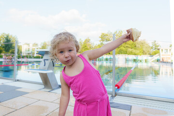 A little girl holds a piece of bread in her hand after swimming in the pool.