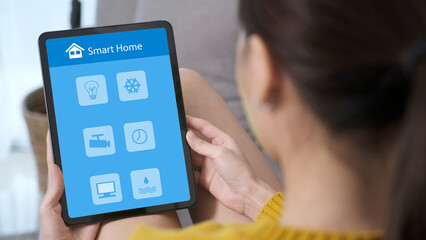 Hand using digital tablet with smart home control icon on screen while sitting on sofa at home, smart home control concept