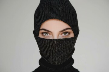 Wall Mural - A woman wearing a black knitted balaclava looks directly at the camera. AI.