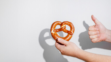 A hand giving a thumbs up while holding a pretzel, symbolizing enjoyment of Oktoberfest traditions and festive snacks