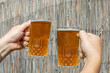 © fotoworld - Two hands clinking beer mugs together outdoors, celebrating Oktoberfest