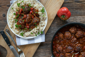 Meatballs in a delicious spicy sauce. Served with brown rice. Homemade food on rustic and wooden table background