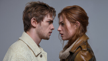 A close-up of a young couple intensely staring into each other's eyes, conveying a moment of emotional tension, passion, or confrontation, both dressed in casual jackets.