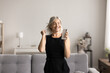 © fizkes - Cheery woman dancing in living room with smartphone in hand, user of digital streaming services app. Overjoyed middle-aged female celebrate great news, relish moment of victory feel unbelievable happy