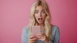© The Little Hut - Blonde young female with pleasant appearance looks with terrified expression in smart phone reads shocking news on webpage isolated over pink background Woman indicates at digital tele : Generative AI