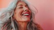 © Boraryn - A joyful older woman with gray hair laughing against a soft pink background.