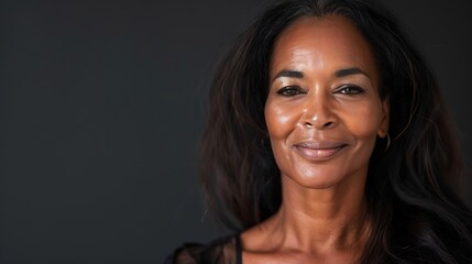 Poster - A close-up portrait of a confident woman with long hair, smiling softly against a dark background.