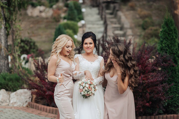 Three women are posing for a picture, with one of them wearing a wedding dress. The other two women are standing behind her, and they are all smiling. Scene is happy and celebratory