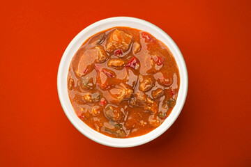 Beef stew with vegetables on red background, top view