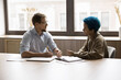 © fizkes - Multiracial colleagues engaged in detailed, focused conversation, serious discussion at conference table, consider issue solution, share opinion, strategy, planning cooperation, take part in teamwork