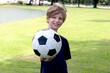 © Stella - Portrait of happy beautiful blonde hair boy holding football in outside garden. Joyful kid with his favorite soccer sport. Athlete child spending time outdoors to play football at public green park.