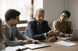 © fizkes - Mature and young teammates negotiate in board room, sit at table, exchanging opinions, listening speech of senior team leader, boss or trainer take part in group briefing, share knowledge and skills