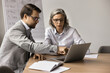 © fizkes - Two businesspeople sitting at table focused on laptop screen, review new platform, software or corporate program, learning together important information, watching and discussing on-line presentation