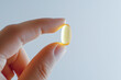 © TinyUU - A hand holding a single, transparent, yellow capsule.  The capsule is illuminated from behind, creating a soft glow.  The background is a simple, muted gray.