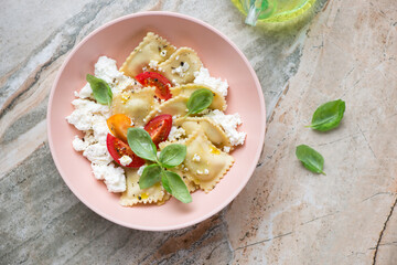 Poster - Italian ravioli served with ricotta, tomatoes and basil, flat lay on a grey and roseate granite background, horizontal shot with space