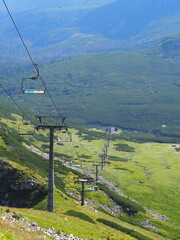 A scenic chairlift spanning over a vast, green valley with distant mountains in the background, offering a beautiful and serene natural landscape view.