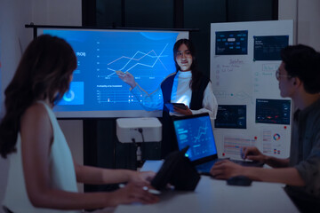 asian leader woman present  business presentation in a dimly lit office, analyzing financial charts and data projections on a screen