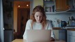 © Wild Dream - Young woman studying at home on a laptop in a cozy kitchen with soft natural light